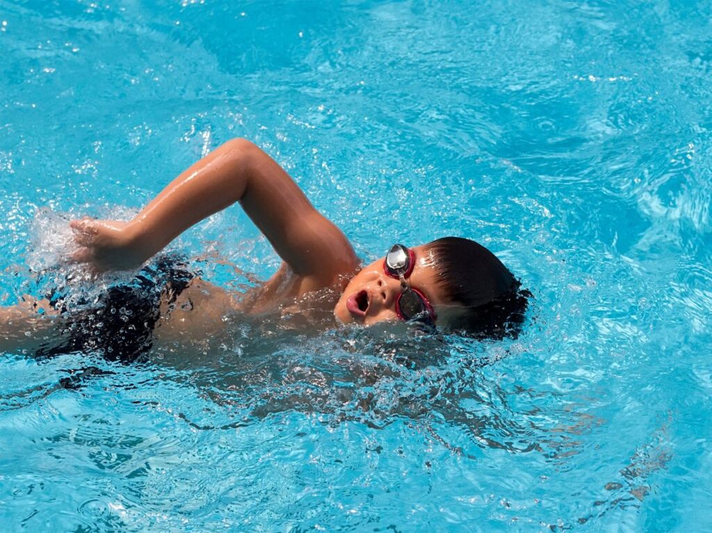 Niño nadando de crol, como profesional en una piscina 