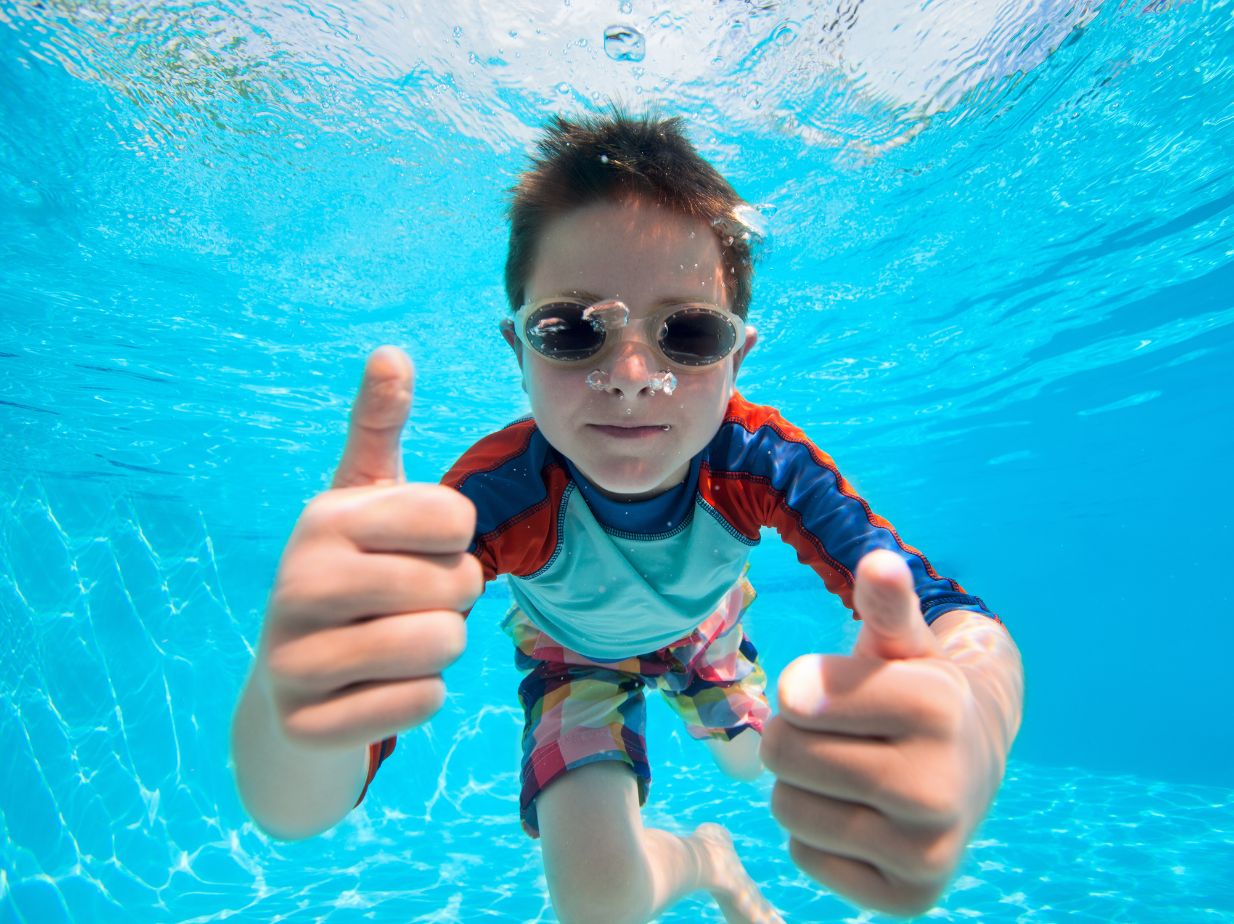 Niño nadando y haciendo una señal con el pulgar, de que lo está pasando bien